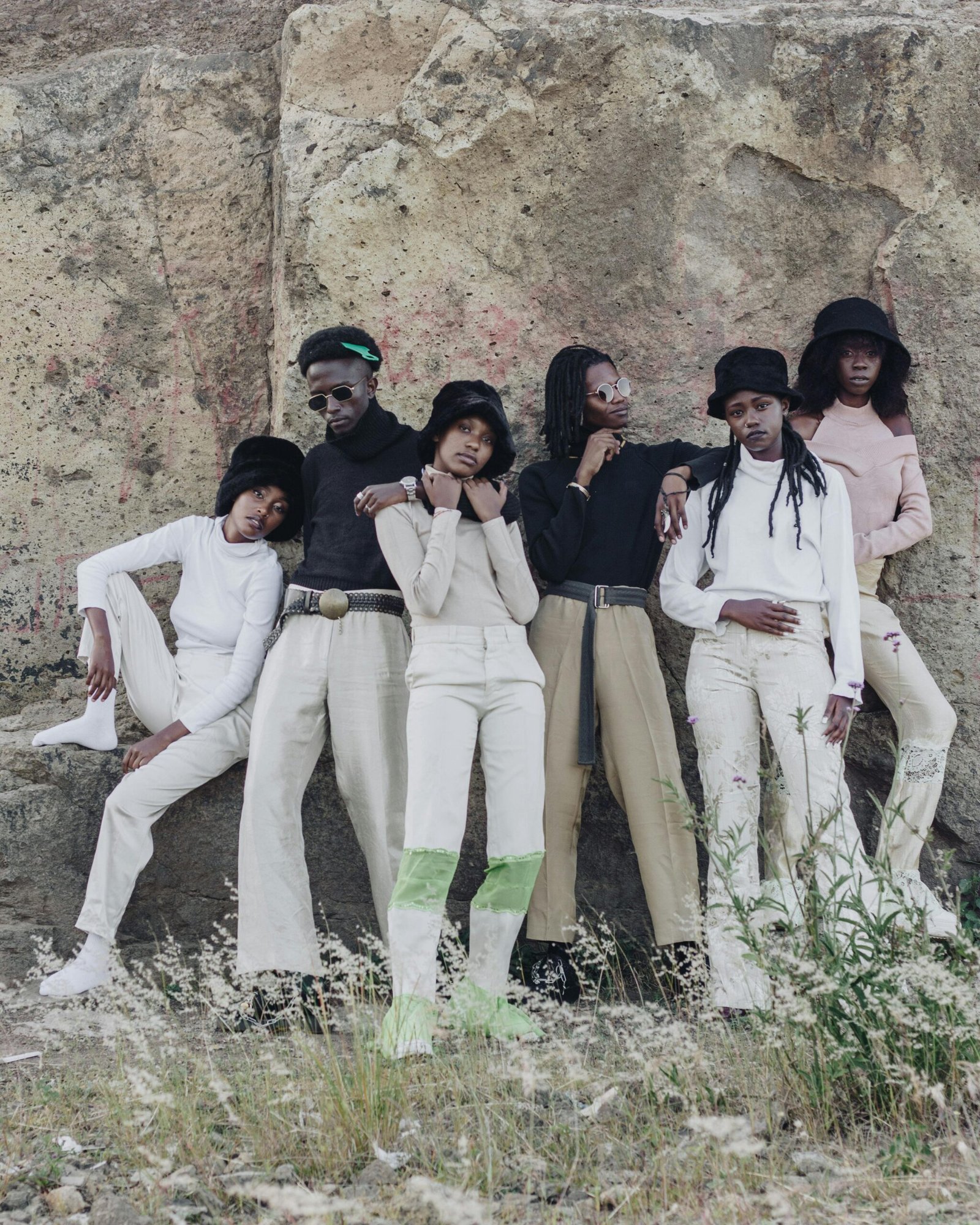 Fashion-forward group posing in trendy outfits by a rock wall in natural scenery.