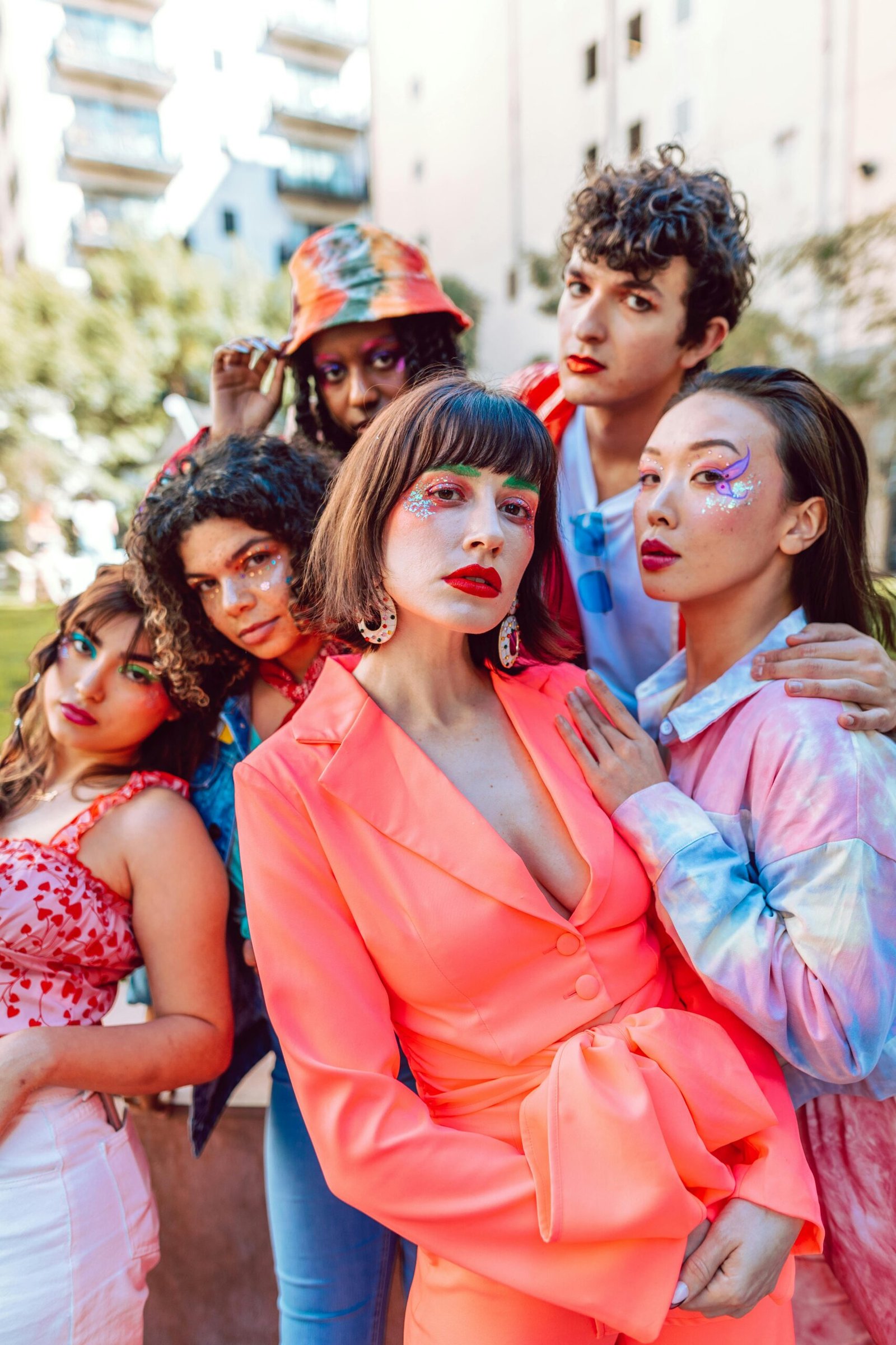 A group of diverse models showcasing colorful fashion and makeup in an outdoor urban setting.